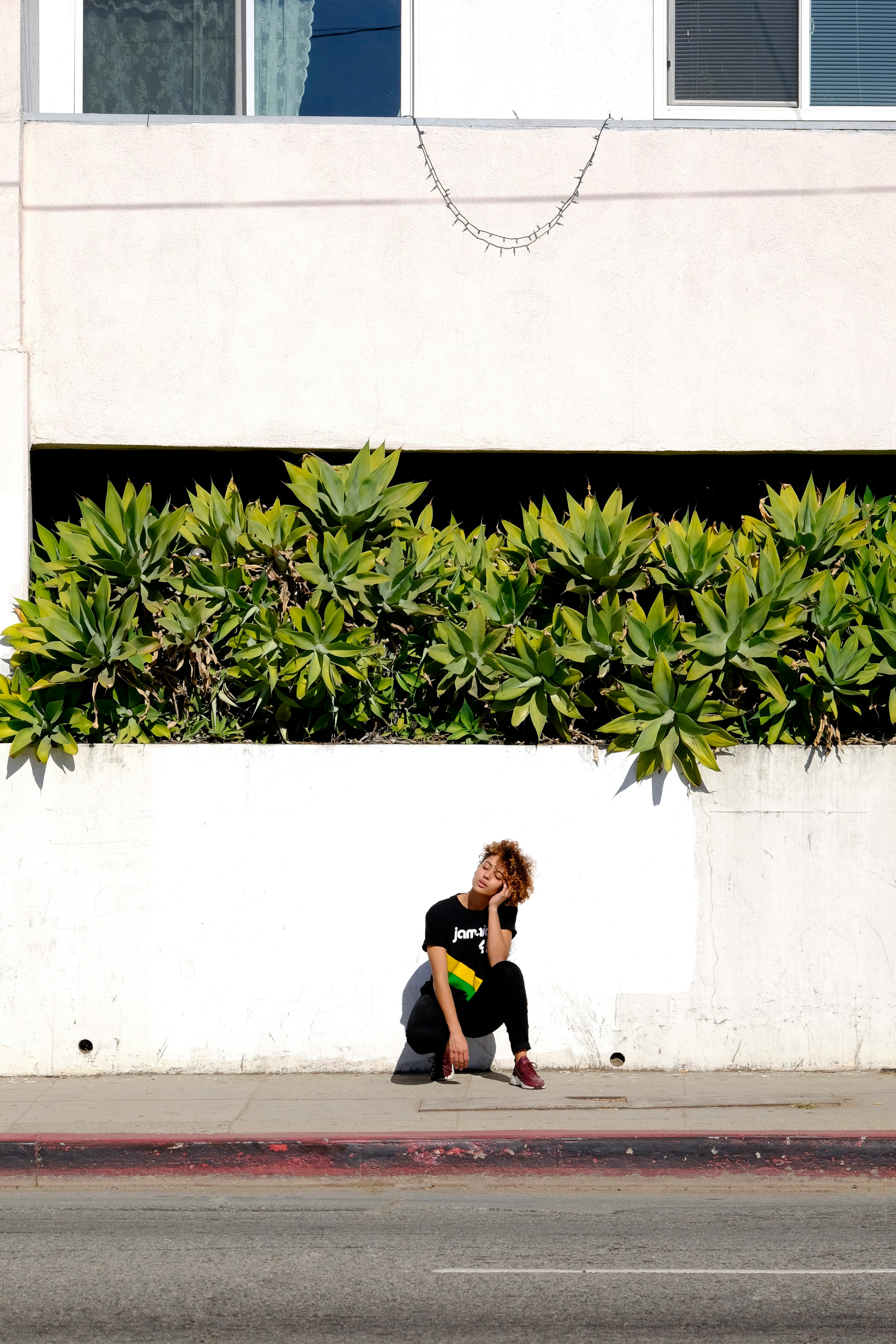 woman sitting near wall with plant